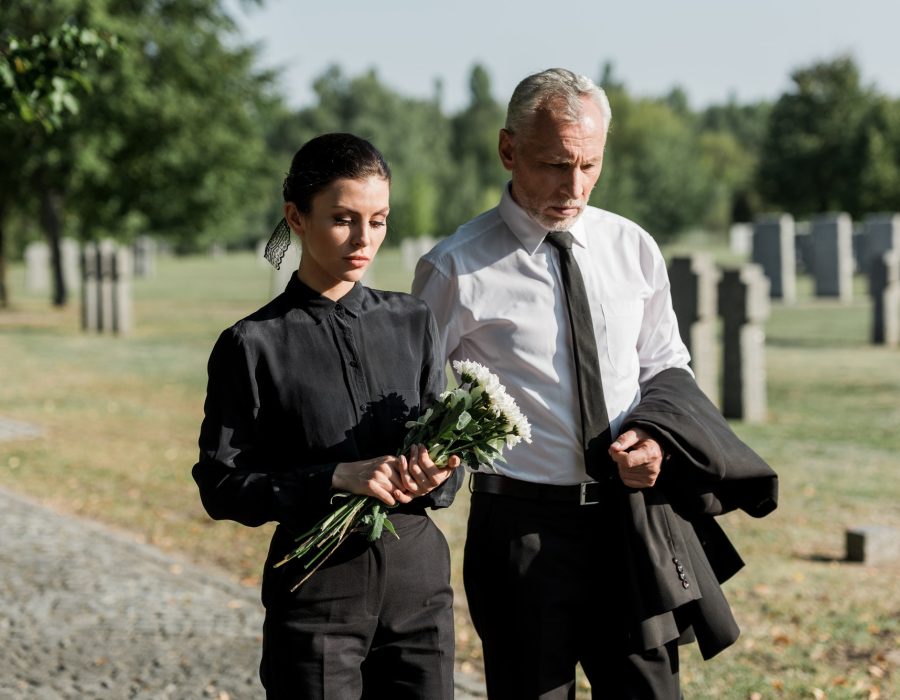 bearded-senior-man-walking-near-woman-with-flowers-on-funeral.jpg